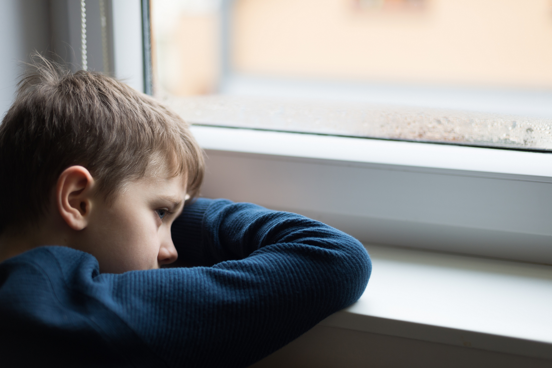 Sad little boy sitting in front of window