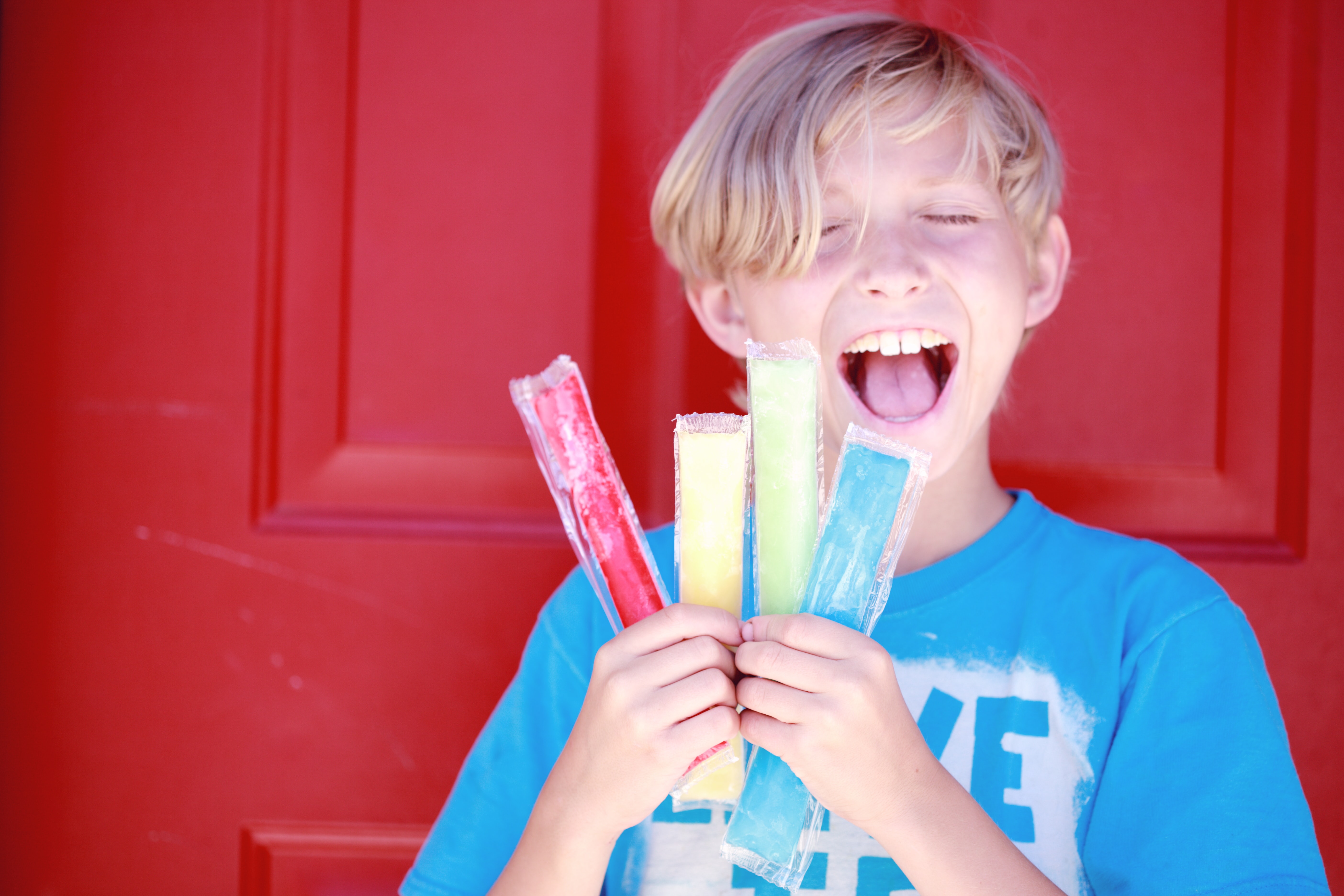 Churchich Recreation Summer Safety for Outdoor Play Happy Boy in Blue Shirt in front of Red Door and Holding Ice Pops